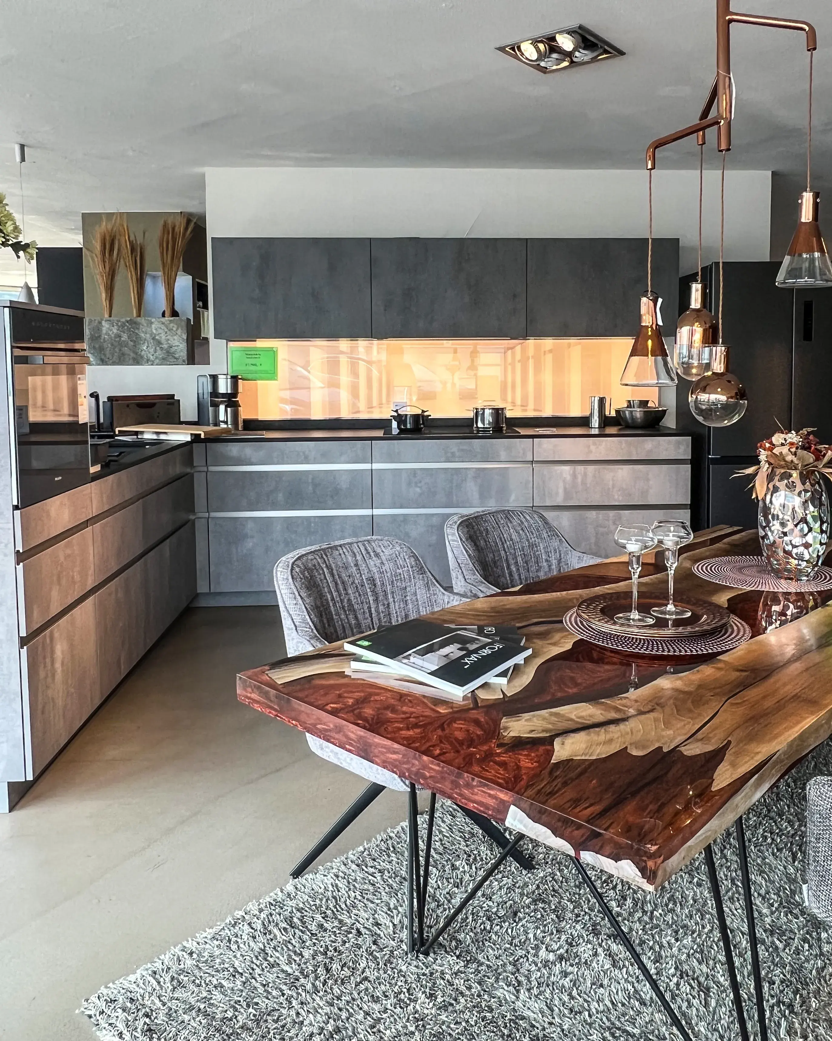 Moderne Küche mit Holz-Esstisch, grauen Stühlen und warmen Pendelleuchten.